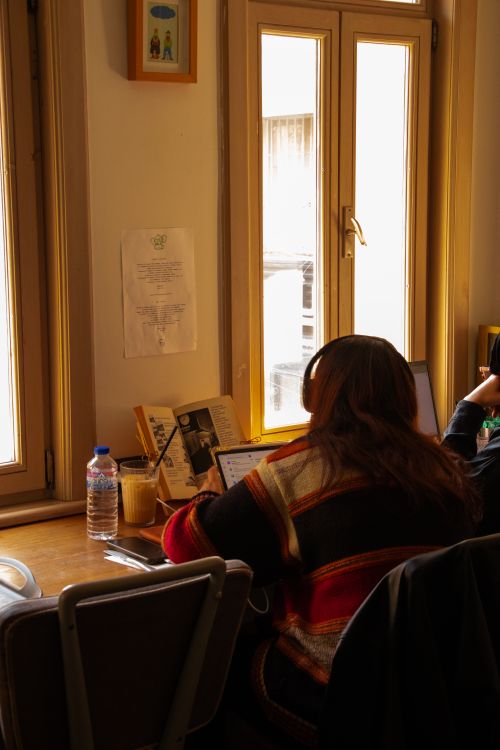 Free A woman wearing headphones works on a laptop by a sunlit window in a cozy room. Stock Photo