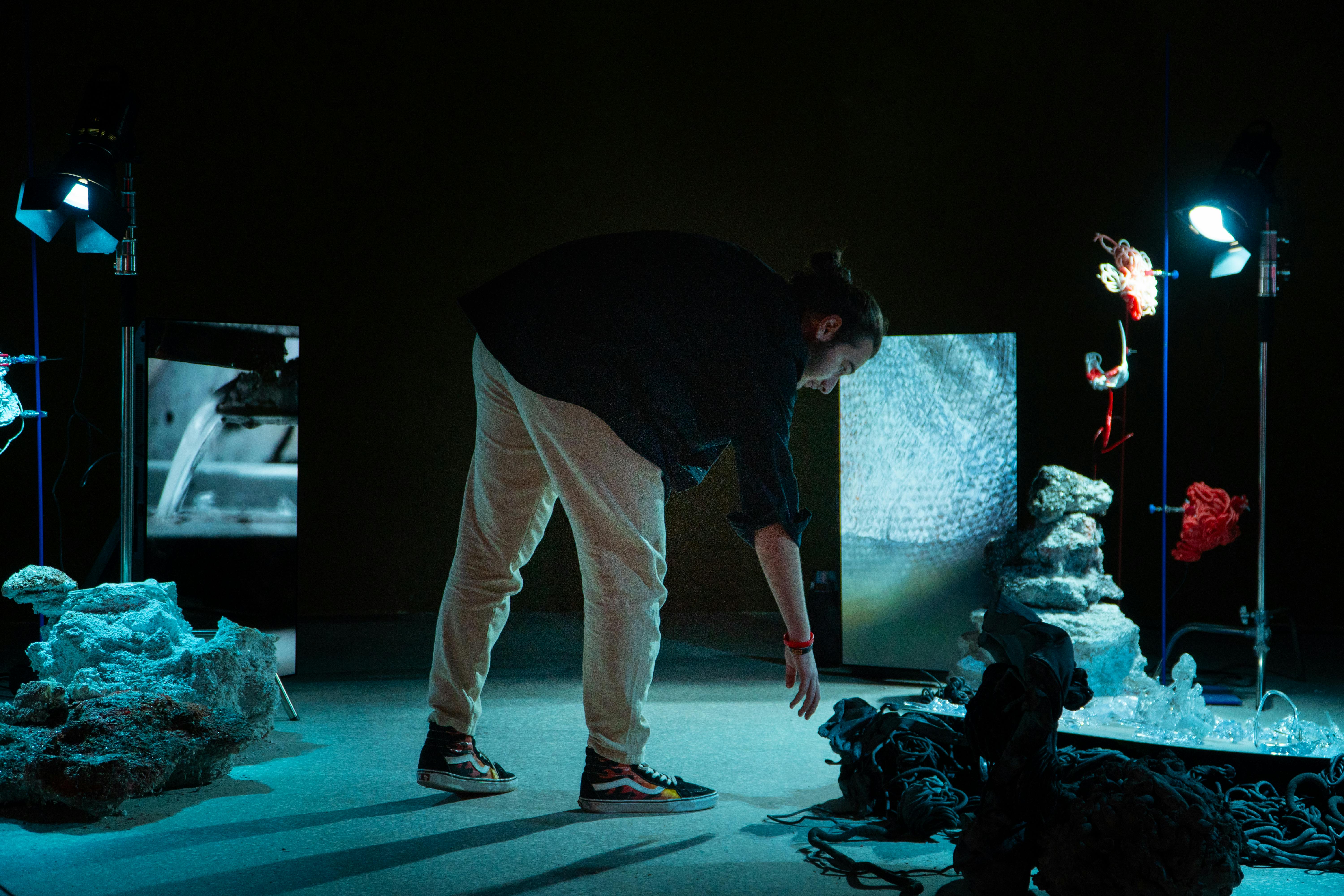 Un homme interagit avec une installation artistique sous un éclairage tamisé, mettant en scène des rochers et des écrans numériques.