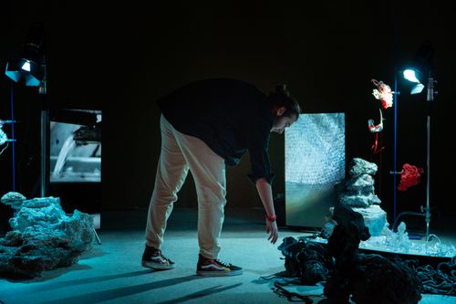 Free A man interacting with an artistic installation under dim lighting, featuring rocks and digital screens. Stock Photo