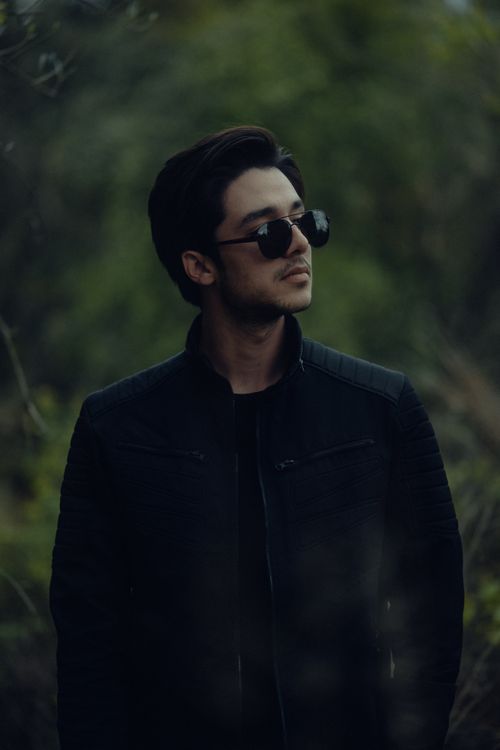 Free Man wearing sunglasses in a dark jacket surrounded by lush greenery. Stock Photo