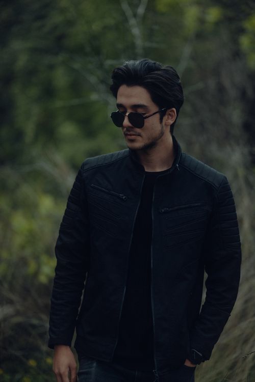 Free Portrait of a man wearing sunglasses and a leather jacket in a natural setting. Stock Photo