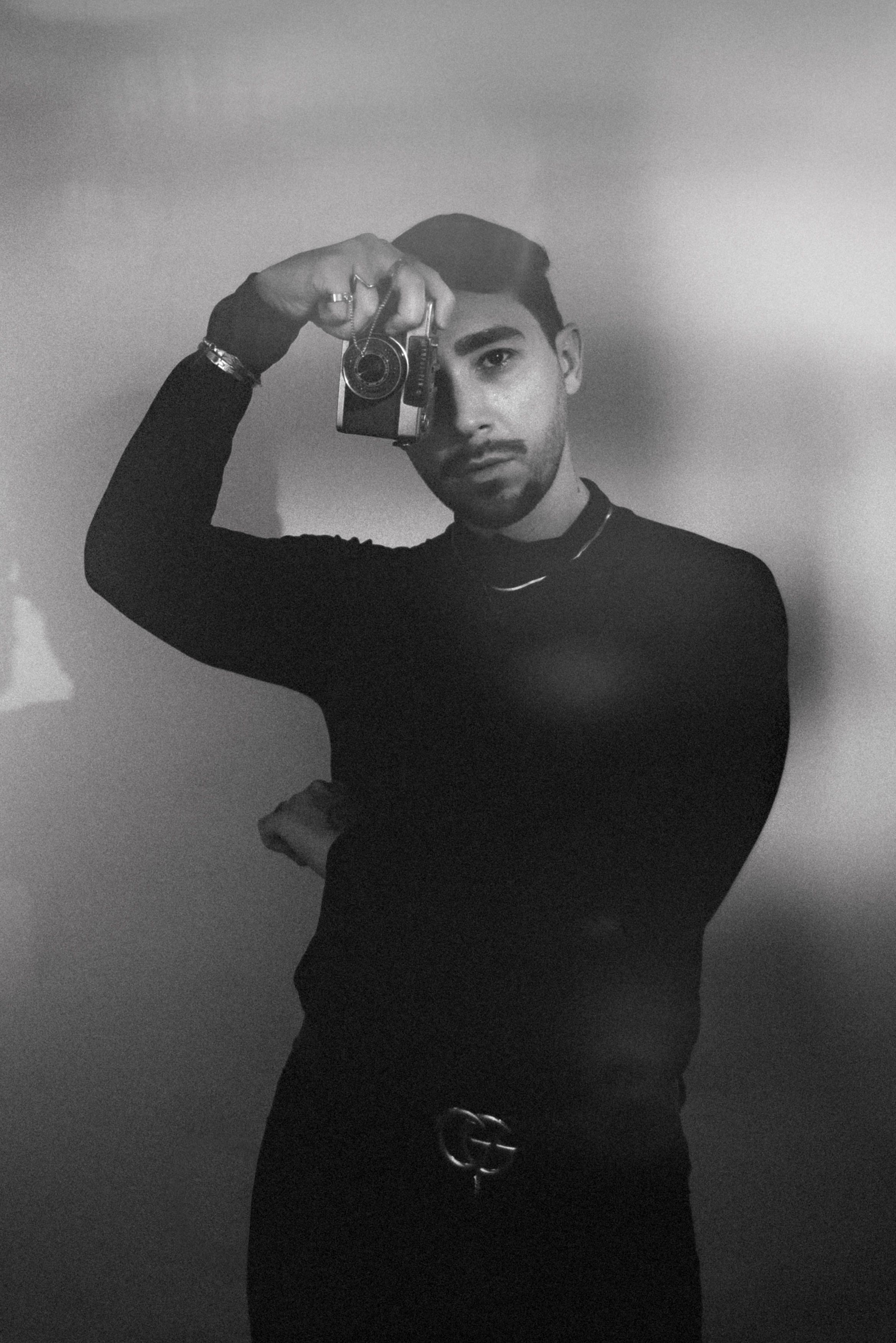 Striking black and white portrait of a male photographer holding a camera, showcasing creativity.
