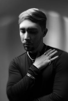 Moody black and white portrait of a young man in a contemplative pose, highlighting facial features.