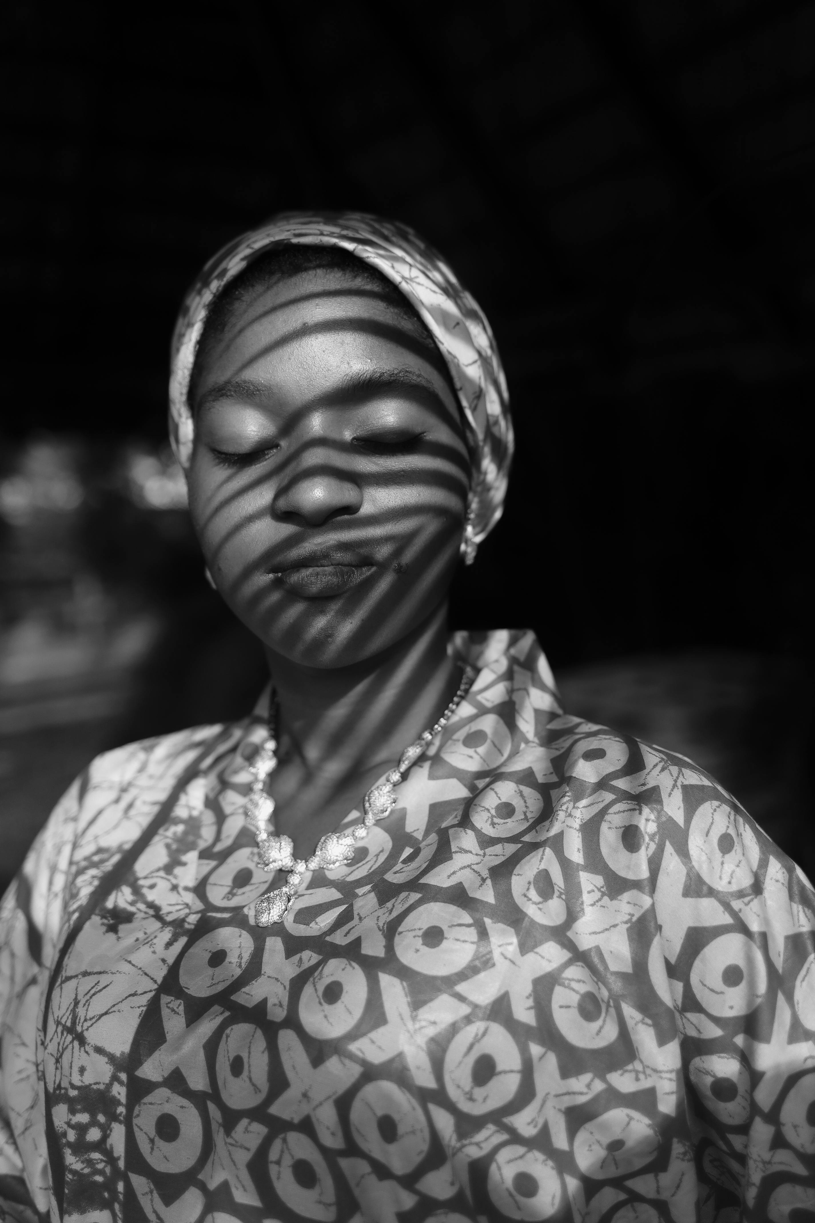 Artistic black and white portrait with shadows creating striped patterns on a woman's face.