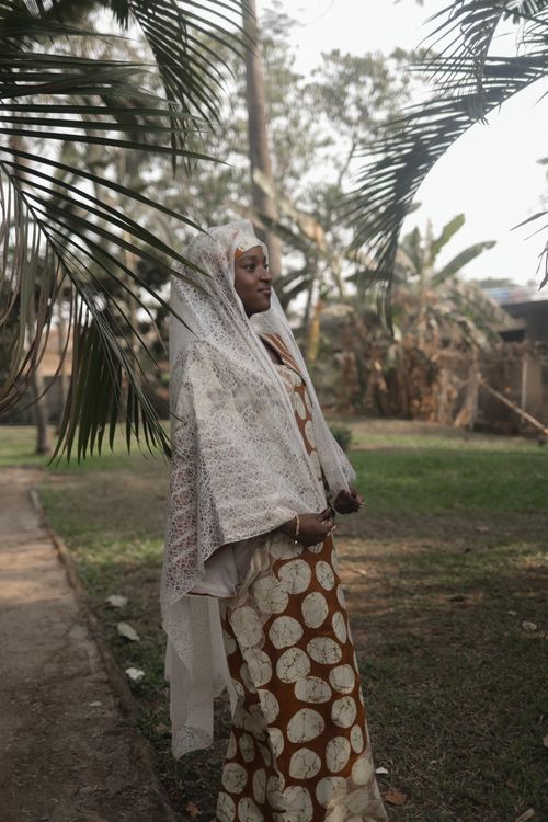 Free Elegant woman in traditional dress standing in a serene outdoor garden setting. Stock Photo