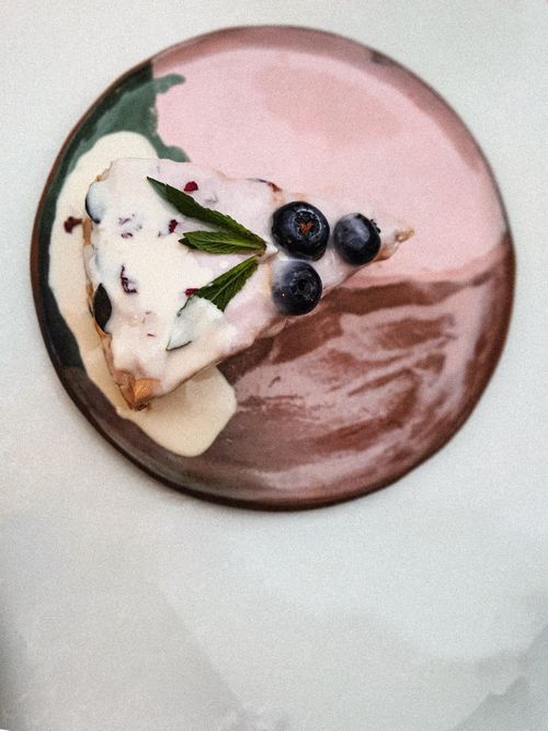 Free Top view of a delicious blueberry cheesecake slice with mint leaves and cream on an artistic pink plate. Stock Photo