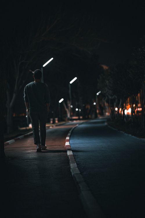 Free Man walking alone at night on a dimly lit path with streetlights. Stock Photo