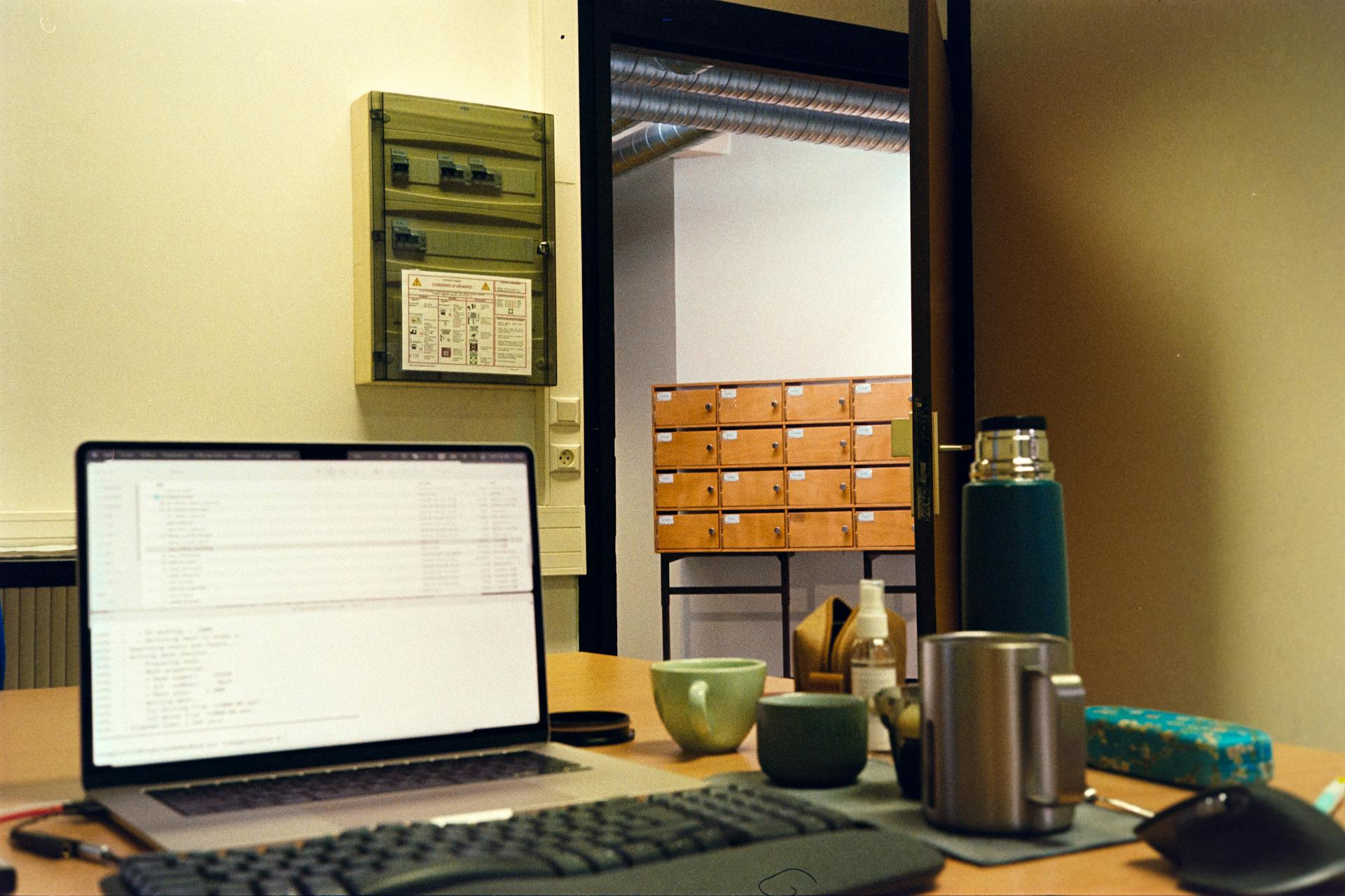 A cozy office workspace featuring a laptop, mugs, and storage drawers in a warm setting.