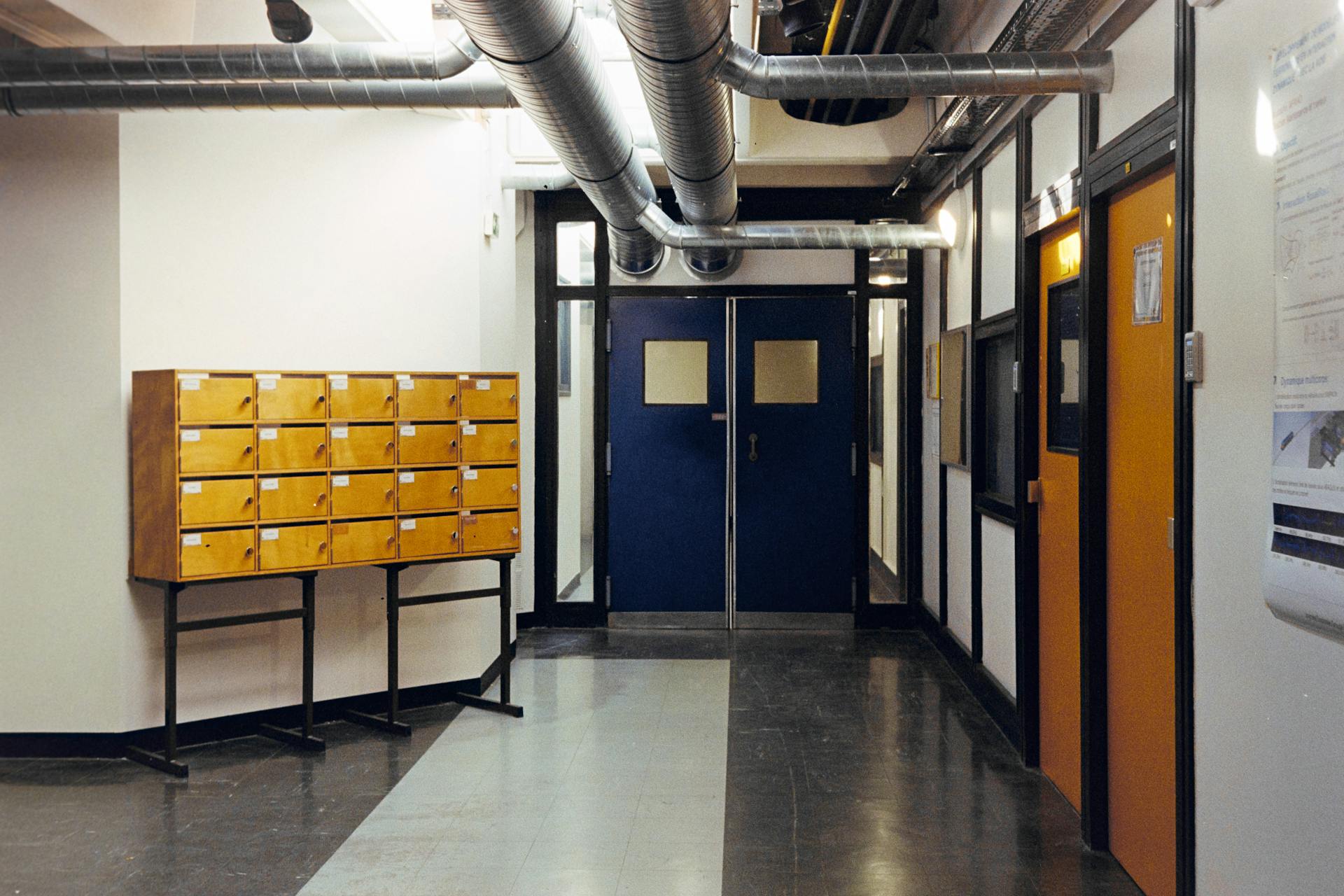 Industrial hallway in Compiègne, France, featuring metal ducts and wooden lockers.