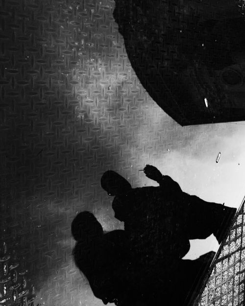 Free Black and white reflection of a person in a puddle on a textured urban street. Stock Photo