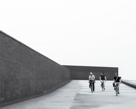 Three people biking along a minimalist urban path, showcasing modern architecture.