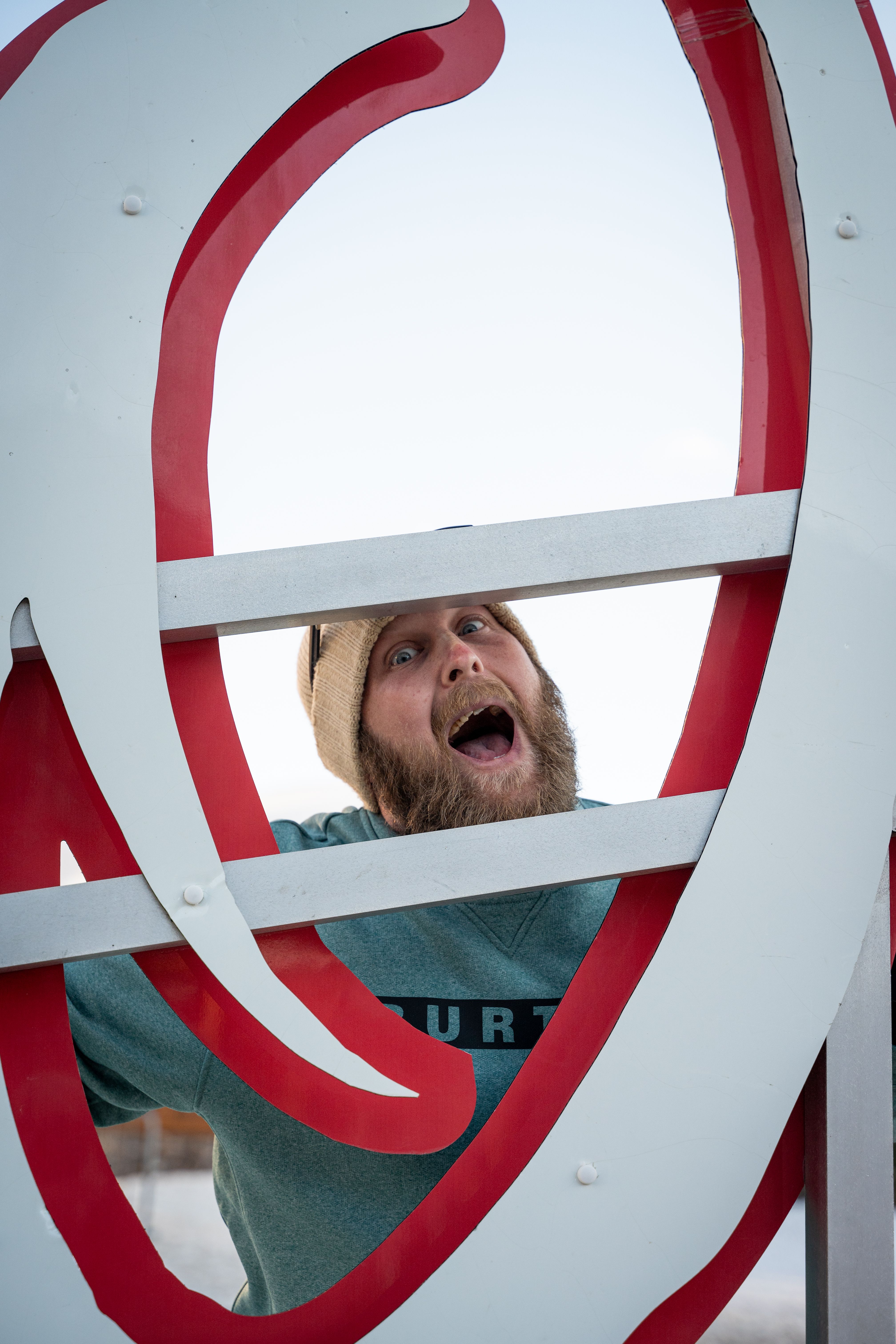 Adult male with beard joyfully posing behind a large outdoor sign.