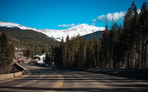 Free Open highway through forested mountains with snow-capped peaks under clear blue sky. Stock Photo