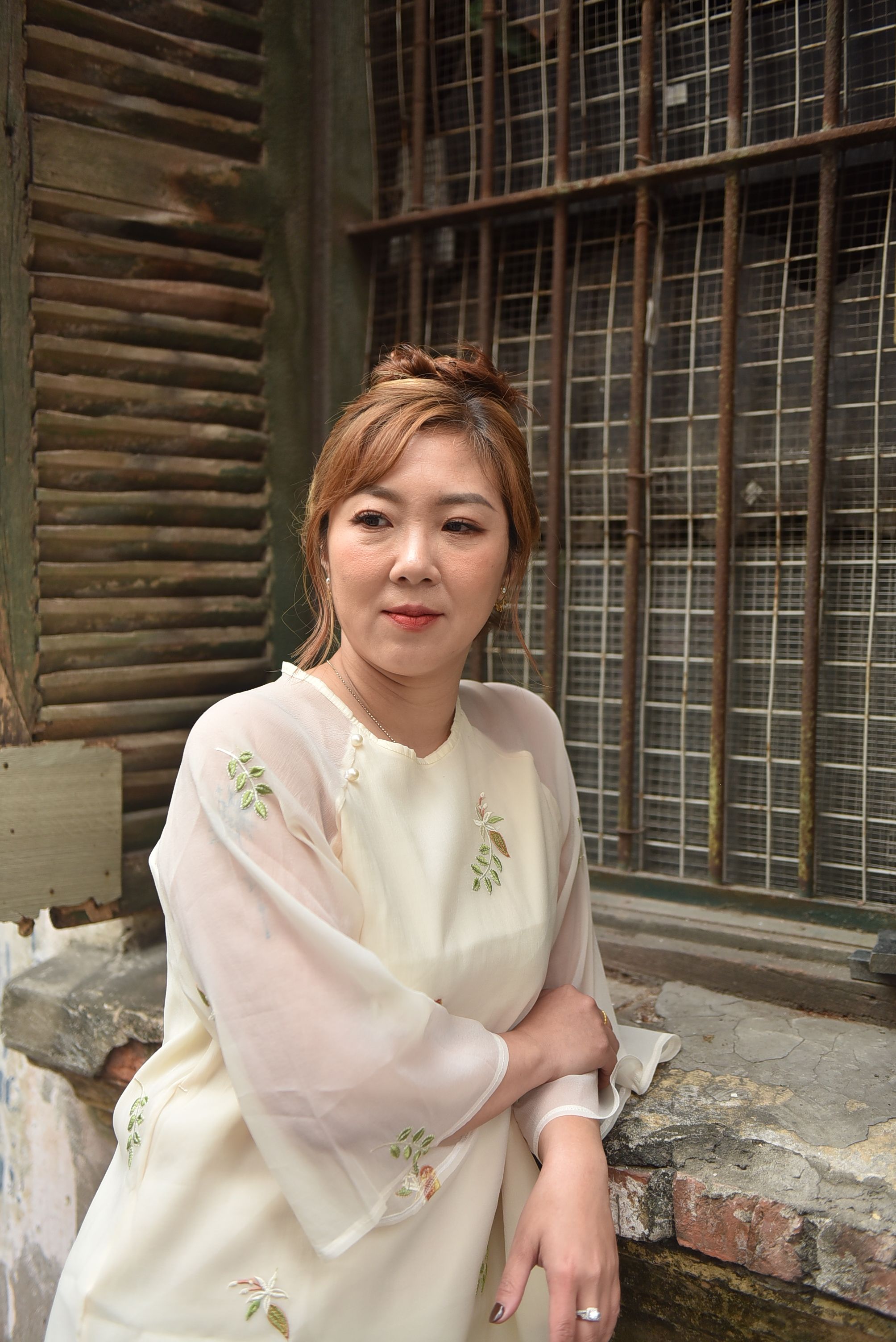 Elegant woman in vintage outfit leaning on shuttered window outdoors.