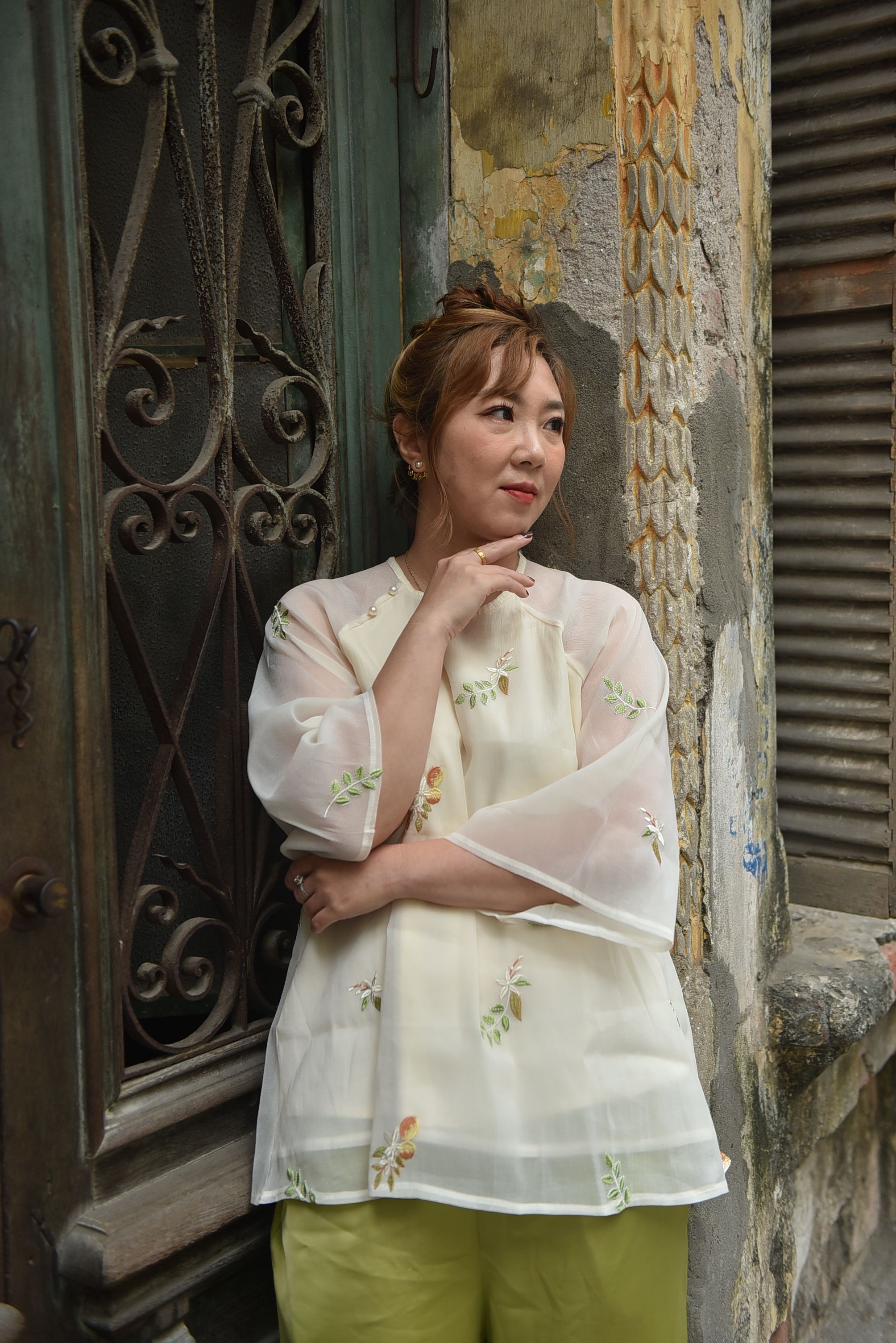 Stylish woman in white blouse poses by an antique door. Contemporary fashion meets vintage charm.