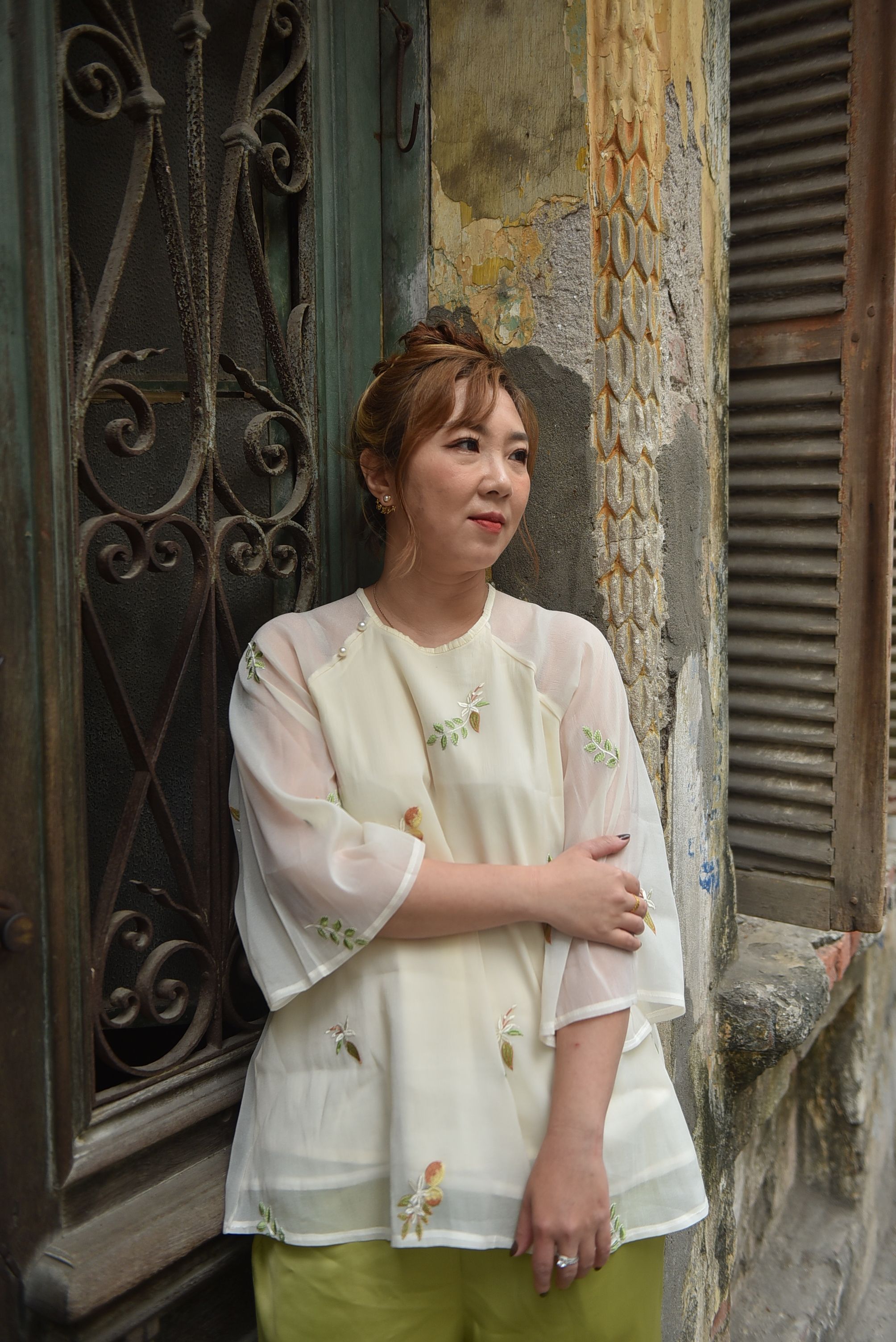 Young woman in a vintage outfit stands by a rustic building, evoking nostalgia.