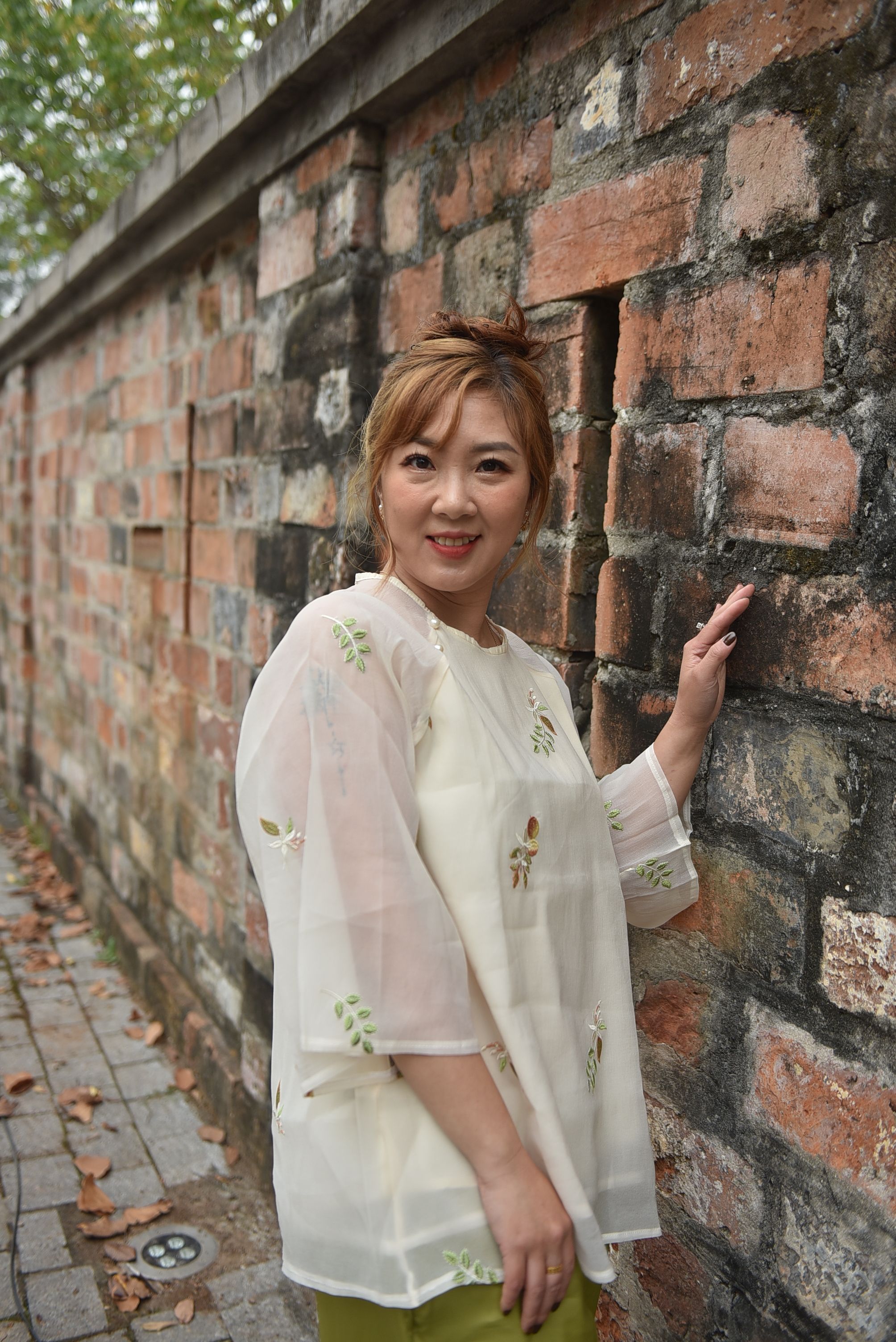 Smiling Woman Posing by a Rustic Brick Wall Outdoors · Free Stock Photo