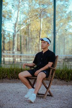 Casually dressed young man sitting in a chair outdoors with trees in the background.