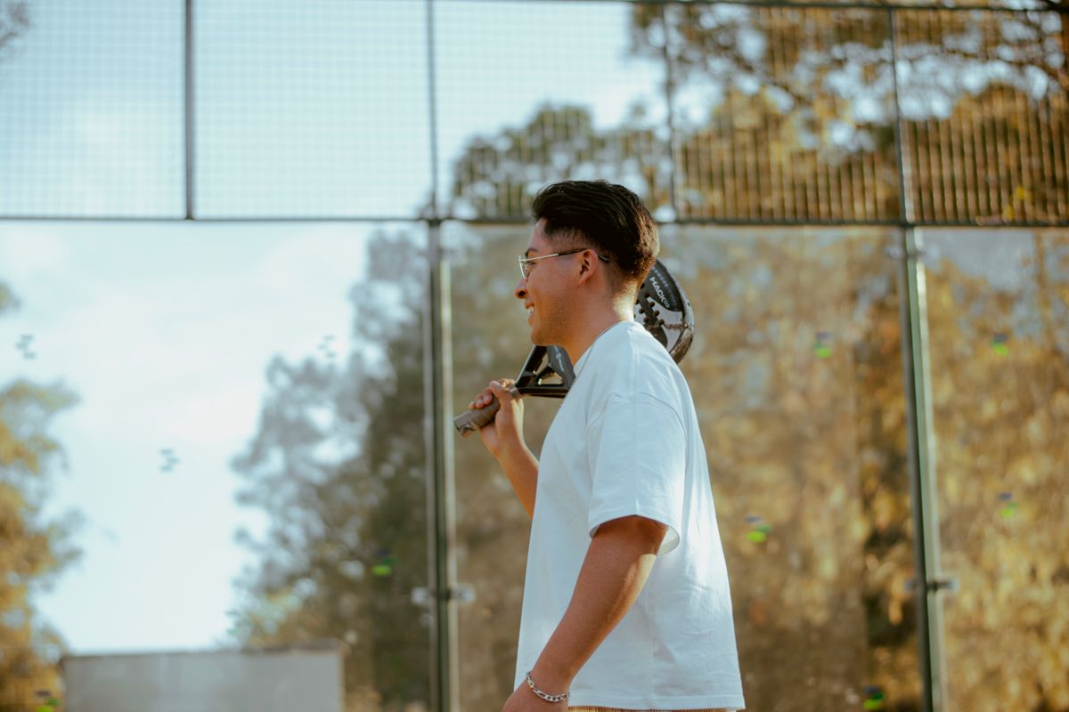 A young player with his racket over his shoulder looks out across an outdoor court