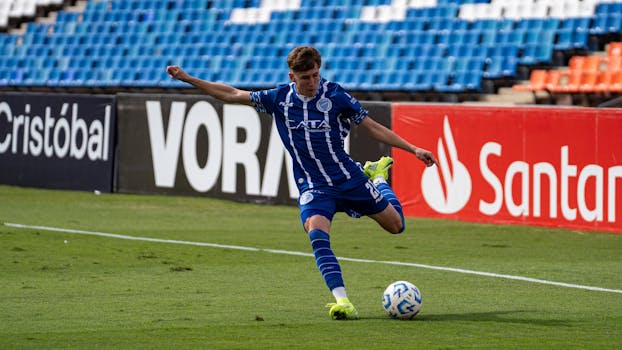 Athlete in blue uniform kicking soccer ball on outdoor stadium field.