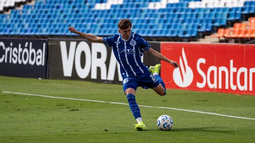 Free Athlete in blue uniform kicking soccer ball on outdoor stadium field. Stock Photo