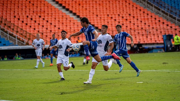Soccer players competing in a dynamic match on a green field with stadium seating.