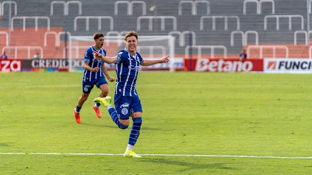 Two soccer players in blue jerseys celebrate a goal during a match on a bright day.