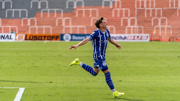 A soccer player in blue uniform celebrates after scoring a goal during a daytime match.