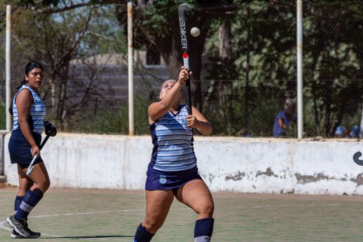 Two women playing field hockey outdoors in action with equipment.