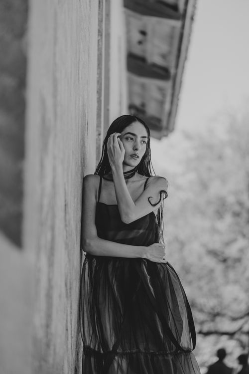 Free Black and white portrait of a woman in a sheer dress leaning against a wall outdoors. Stock Photo