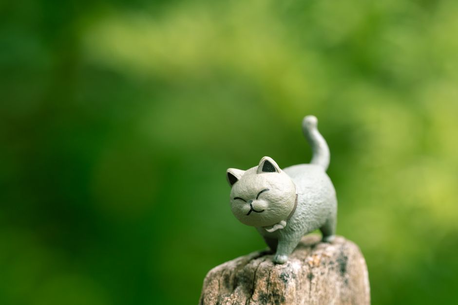 Charming cat sculpture perched on a rock with vibrant greenery backdrop.
