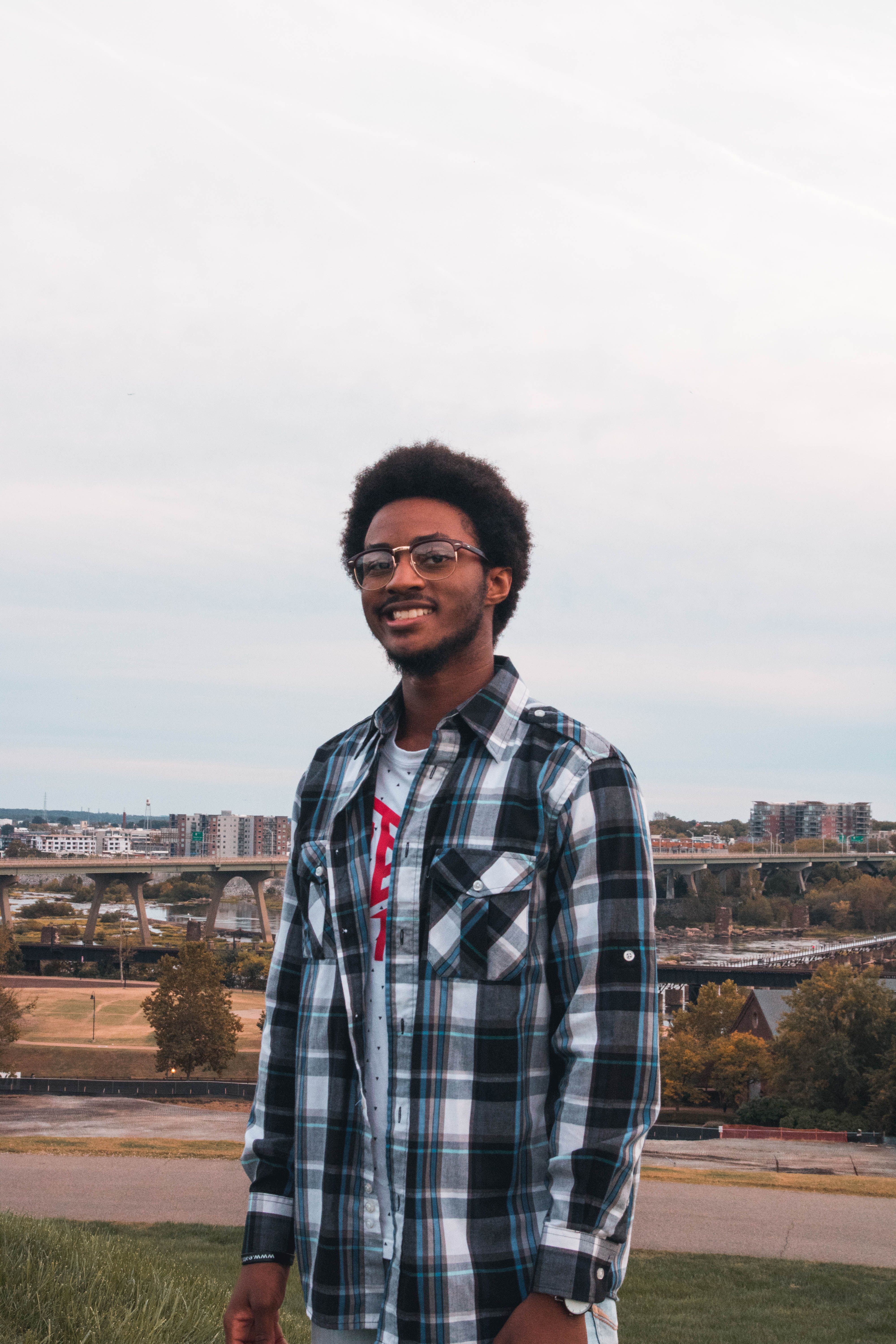 Portrait of a smiling young man outdoors in Richmond, VA, with a cityscape backdrop. Casual style and natural expression.