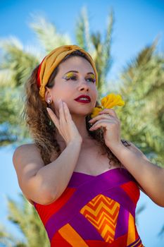 A woman in colorful attire poses with a flower, exuding summer vibes.