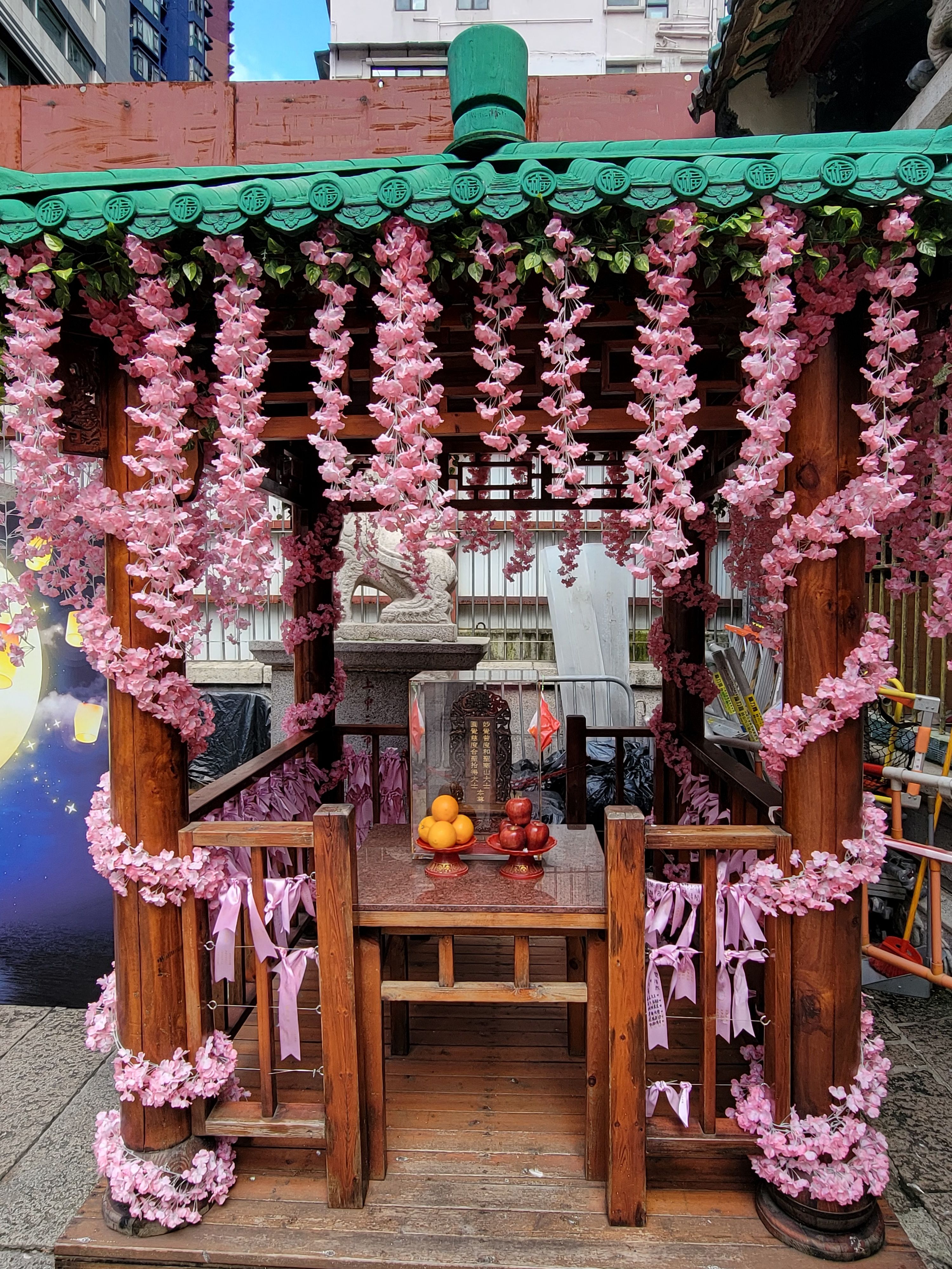 Fotomural Encantador pabellón de madera adornado con guirnaldas florales rosas en un vibrante entorno urbano, Hong Kong
