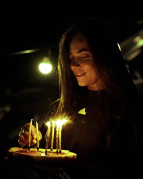 Young woman smiling at a birthday cake with candles at night, creating a warm and intimate atmosphere.