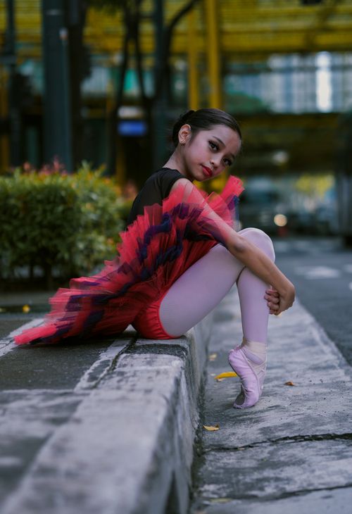 Free Charming young ballerina in vibrant attire poses gracefully on a city street curb, showcasing her artistic flair. Stock Photo
