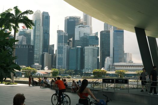 A bustling view of Singapore skyline with people biking and walking, showcasing urban life.