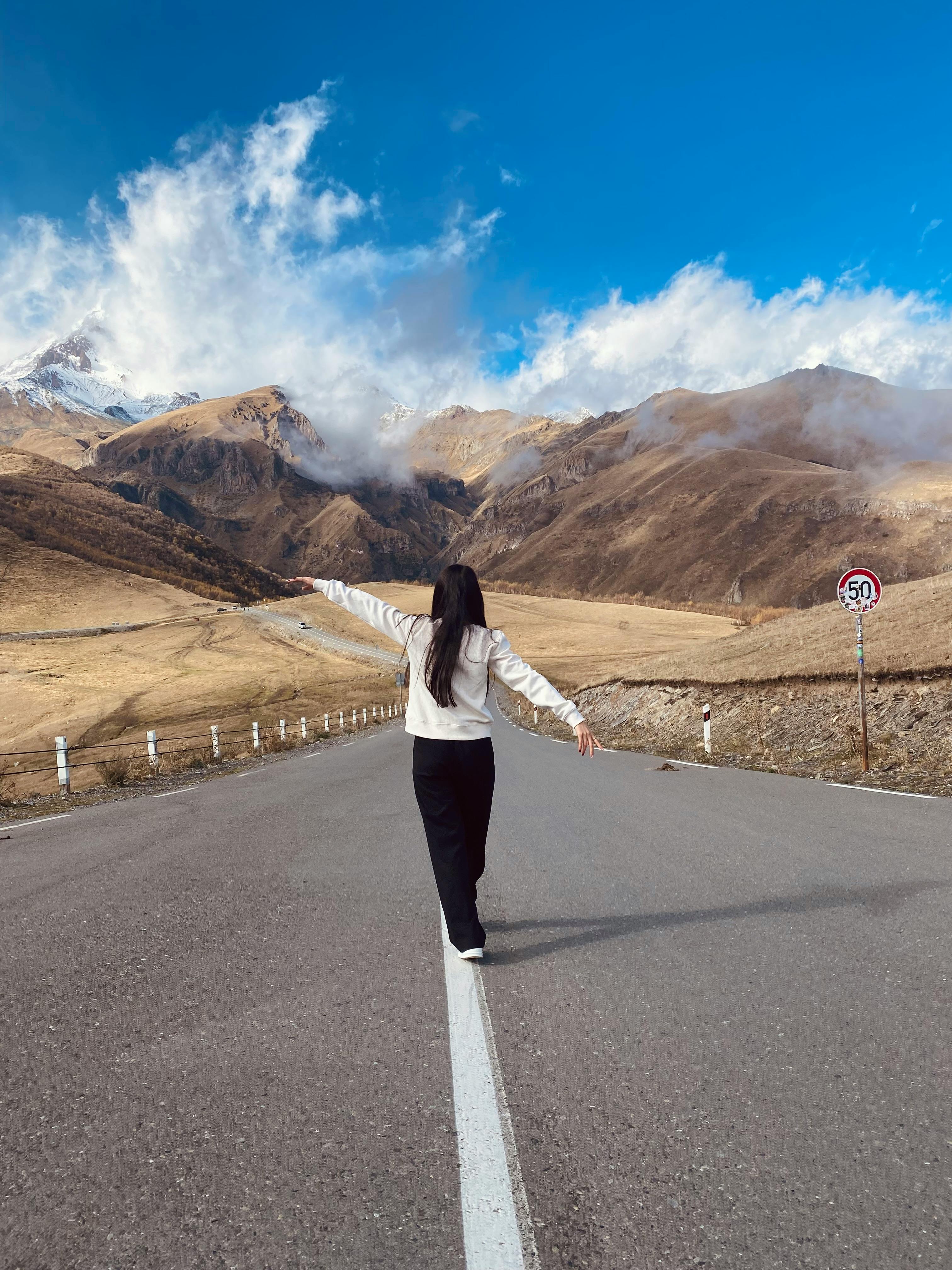 A woman walks freely on a mountain road in Georgia, embracing the natural beauty of the Caucasus.