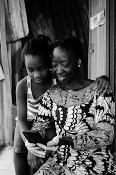 Black and white image of a mother and daughter bonding over a phone outdoors in Abuja, Nigeria.