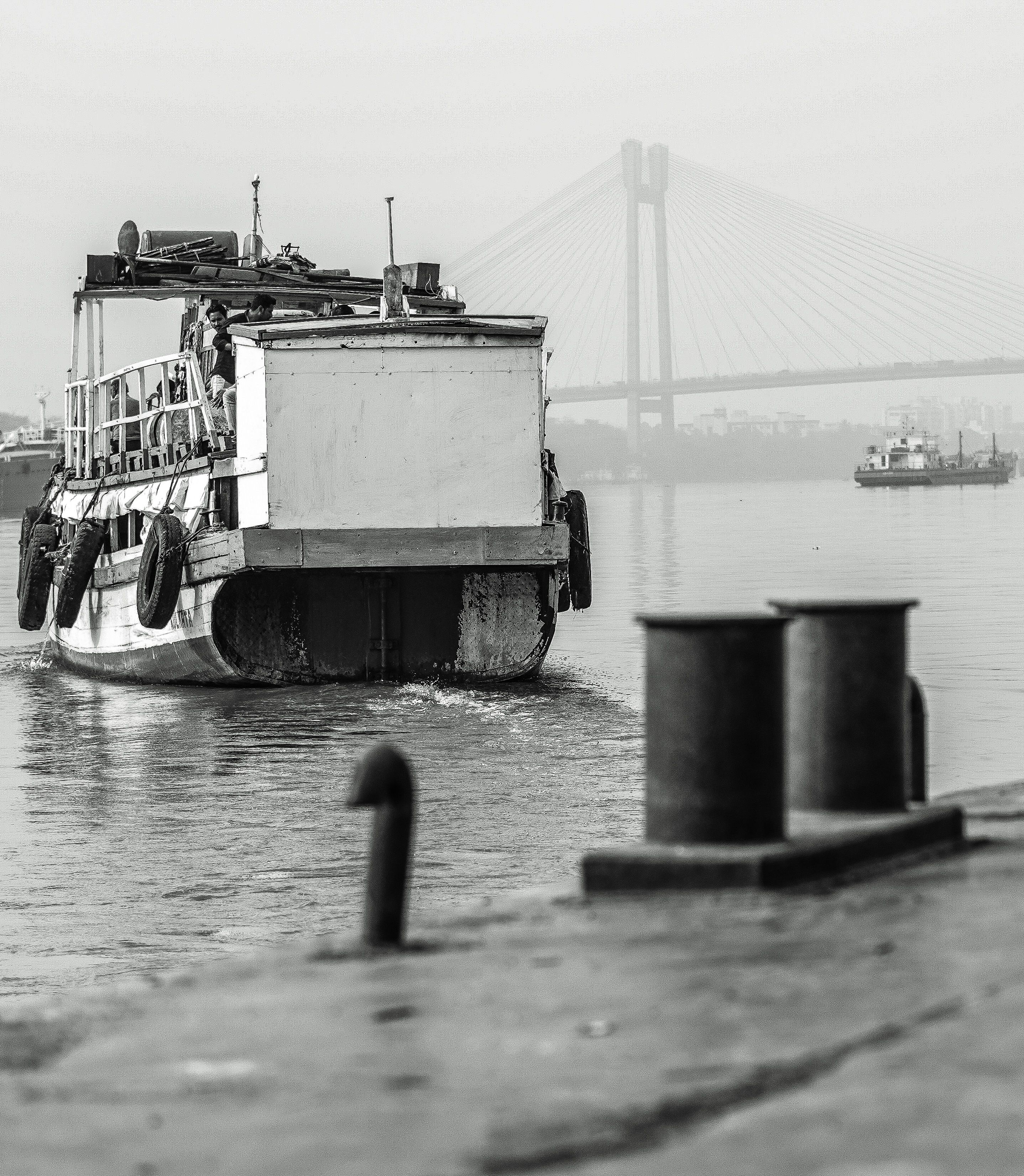 Monochrome view of a riverboat near a suspension bridge, capturing rustic transportation. | Indian Village Development