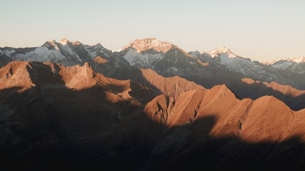 A breathtaking view of a mountain range illuminated by the warm glow of sunset, showcasing snow-capped peaks.