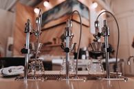 Stainless steel similar drip coffee machine with ribbed filters and transparent glass carafes on table near towel in apartment with artificial light