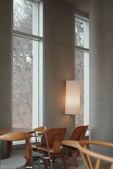 Minimalist cafe interior featuring wooden chairs, large windows, and a soft light fixture.