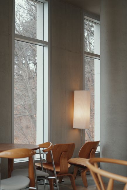 Minimalist cafe interior featuring wooden chairs, large windows, and a soft light fixture.