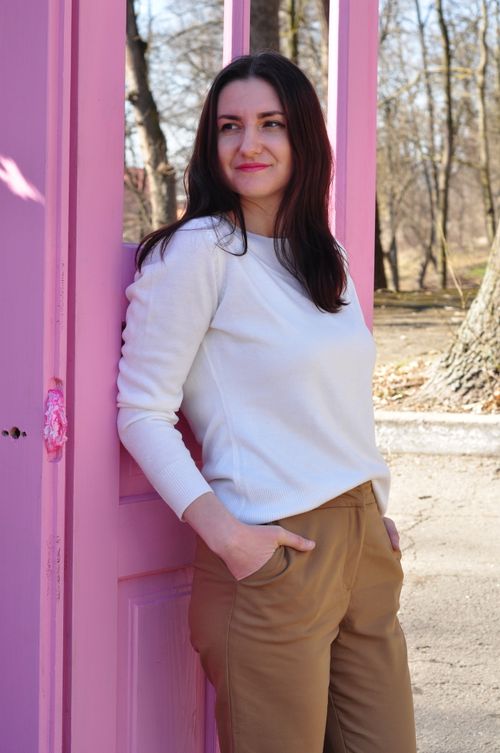 Free Woman in casual outfit leans against a pink door with a serene smile in a sunny spring park. Stock Photo