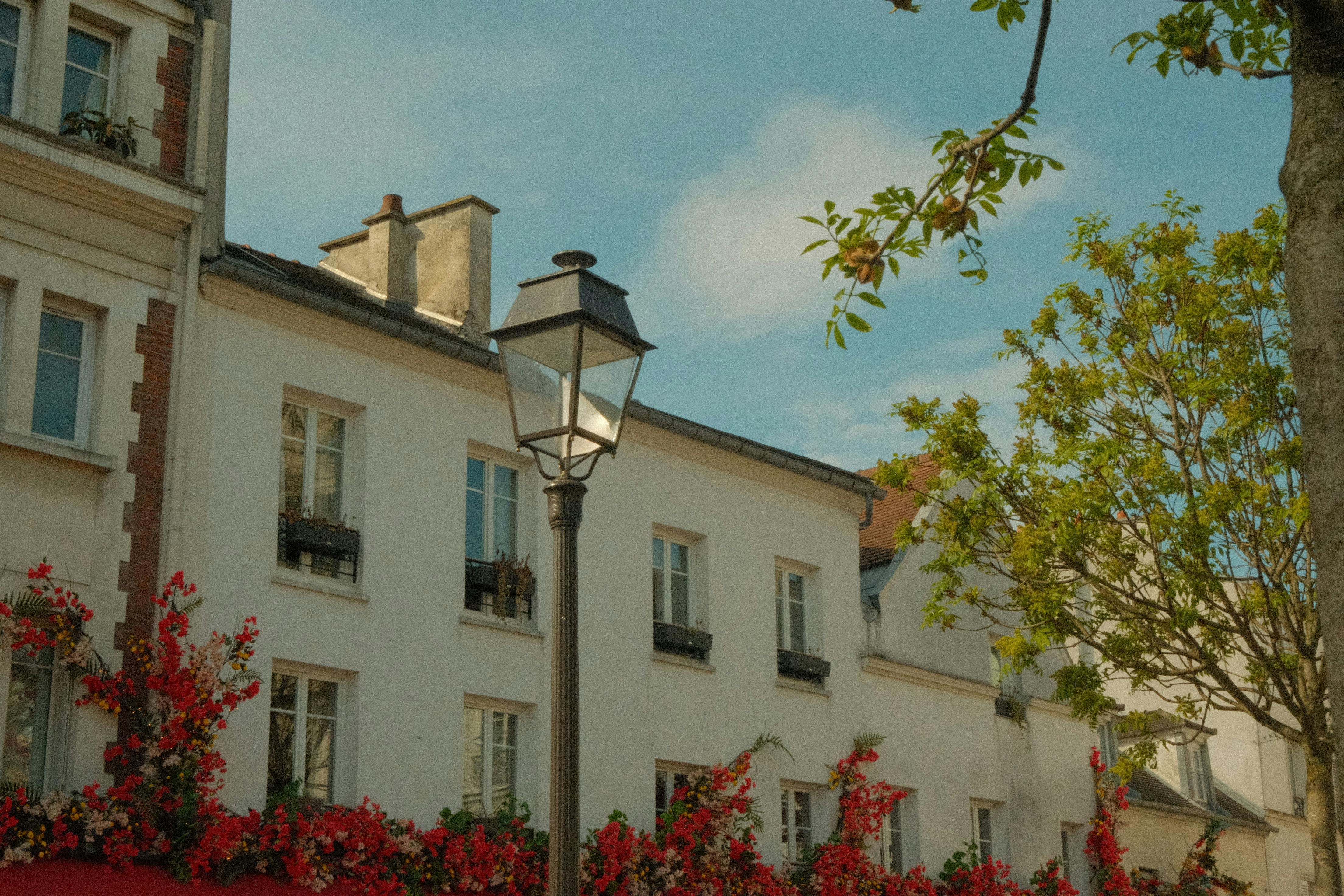 A picturesque European street featuring classic architecture, blooming flowers, and a clear blue sky.