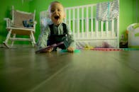 在充满活力的绿色托儿所里，可爱的男婴快乐地爬行在木地板上玩耍