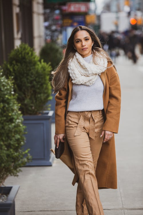 一個女人穿著棕色大衣和褲子在人行道上行走的選擇性焦點