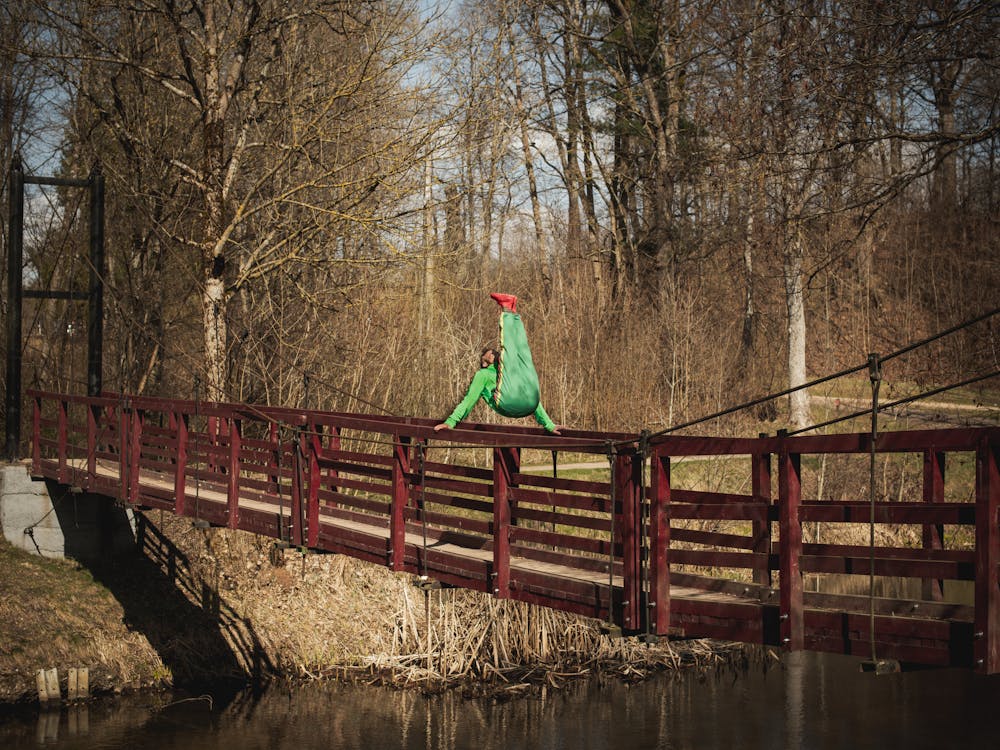 Gratis Un atleta vestido de verde y rojo realiza una pose gimnástica dinámica en un puente al aire libre en Vilnius. Foto de stock