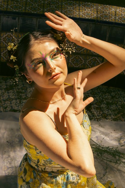 Free A woman with decorative makeup poses gracefully in sunlight wearing a floral dress. Stock Photo